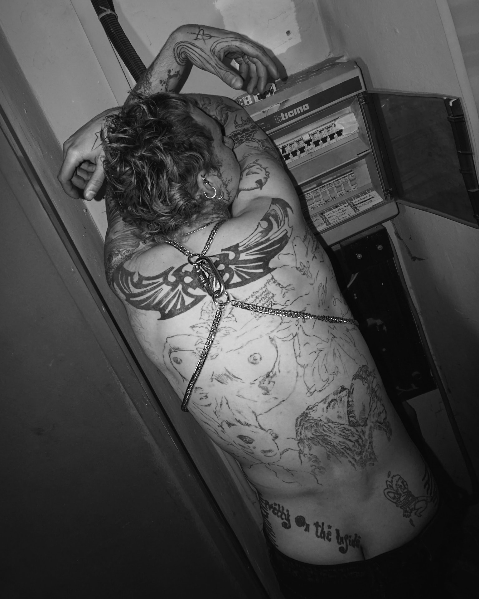 Black-and-white back and body detail, chain jewellery following the spine across tattooed skin