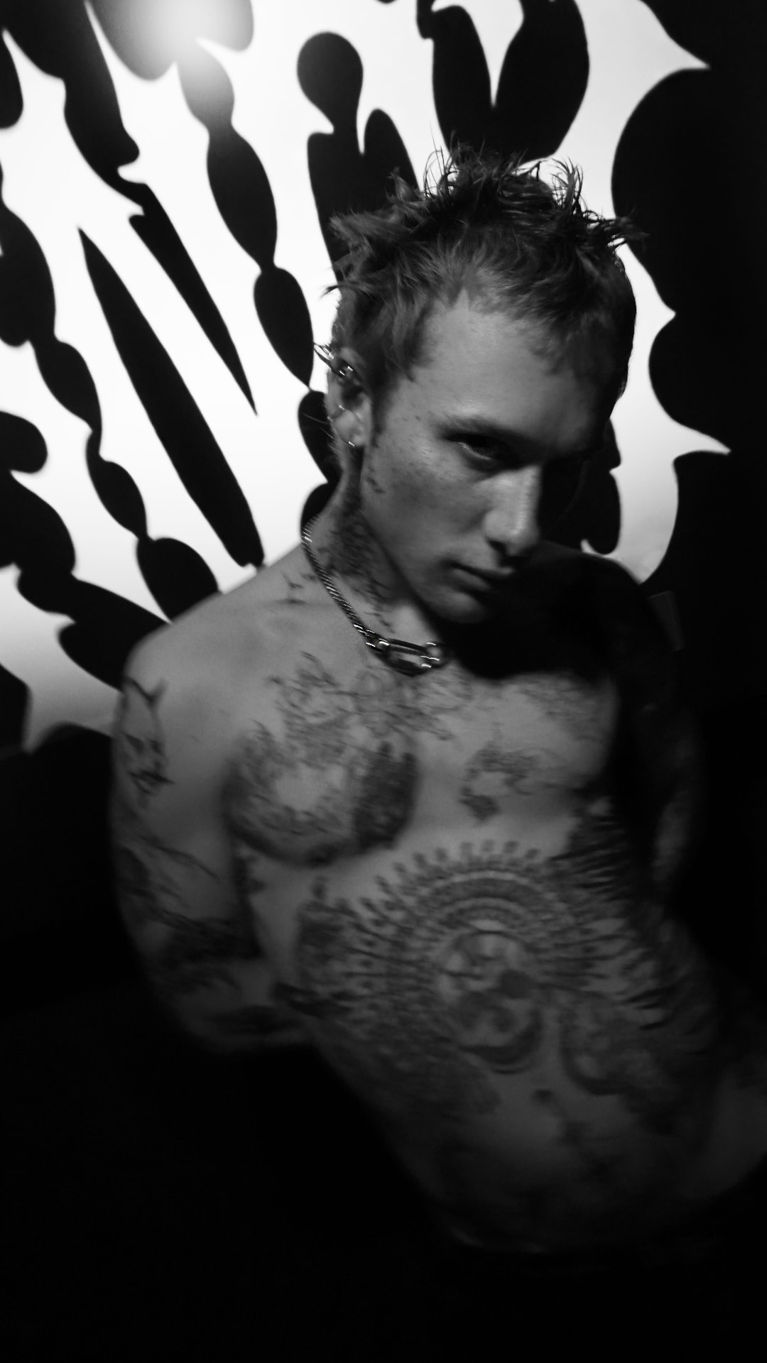 Tattooed male model in black and white, chain necklace at the neck, against the sharp white Knot flame logo backdrop