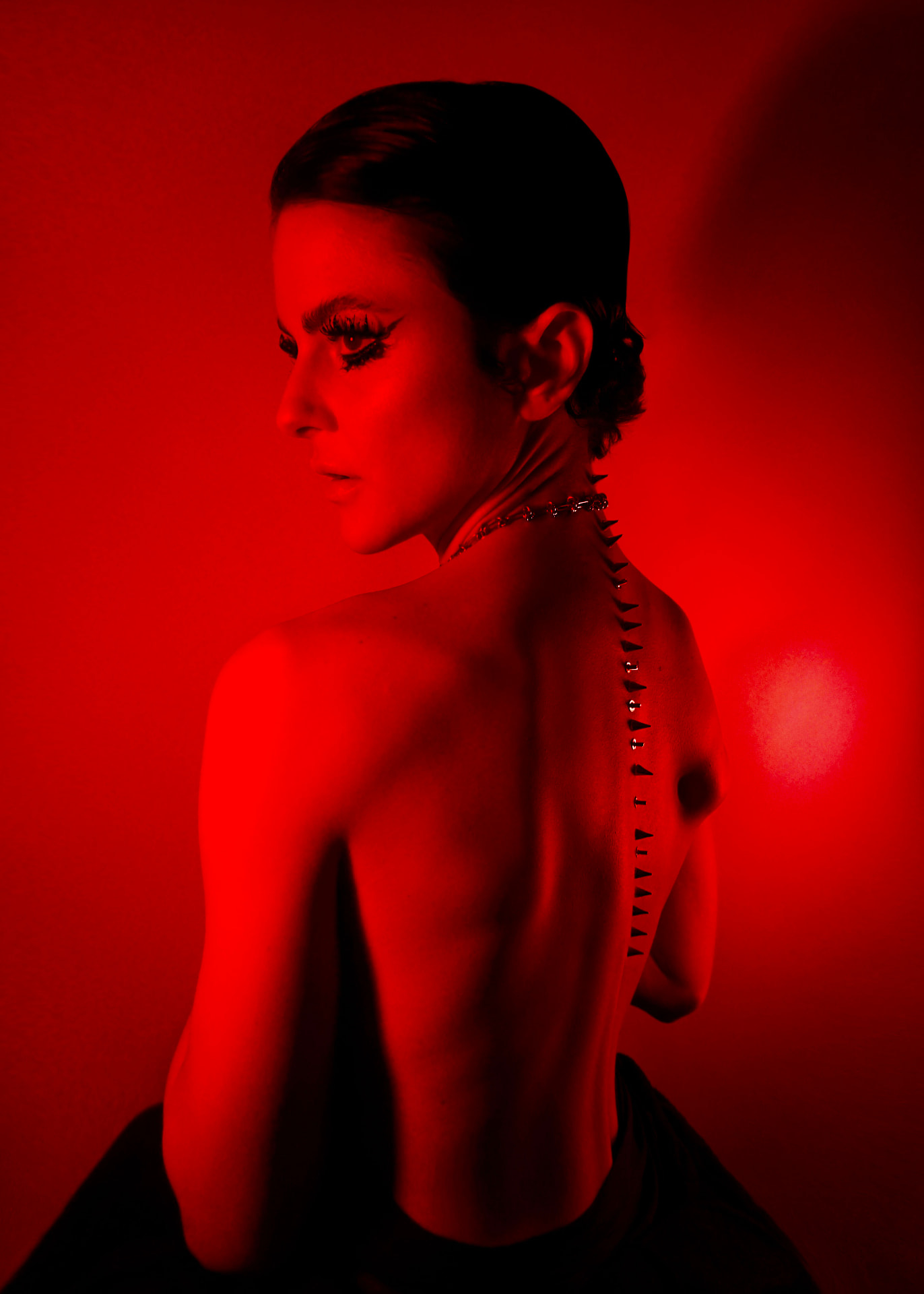 Red-lit back portrait: chain necklace and a row of metal spikes running along the spine