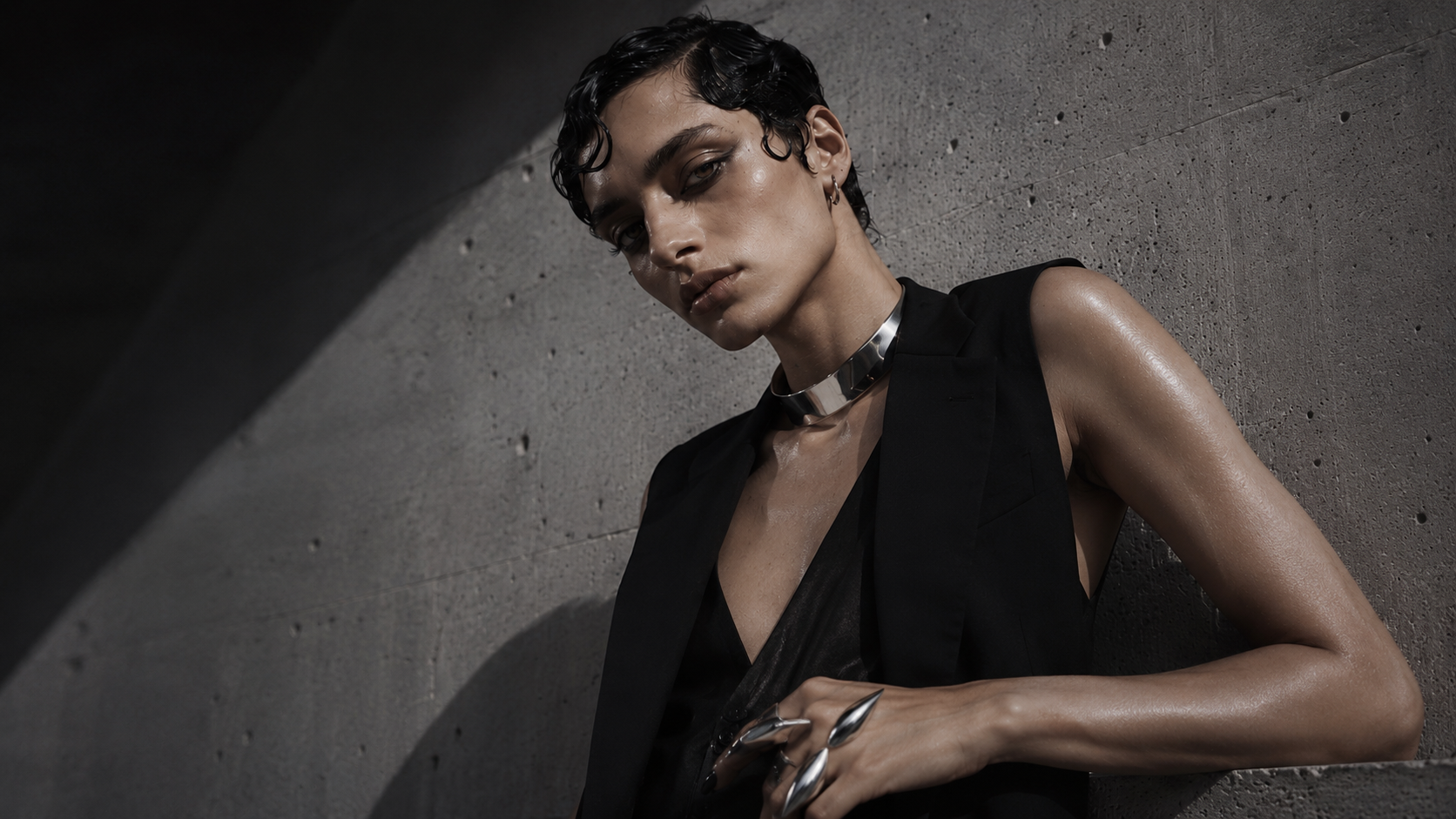 Portrait leaning against raw concrete, chrome collar and silver rings